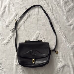 Black handbag with a handle at the top and a long strap
